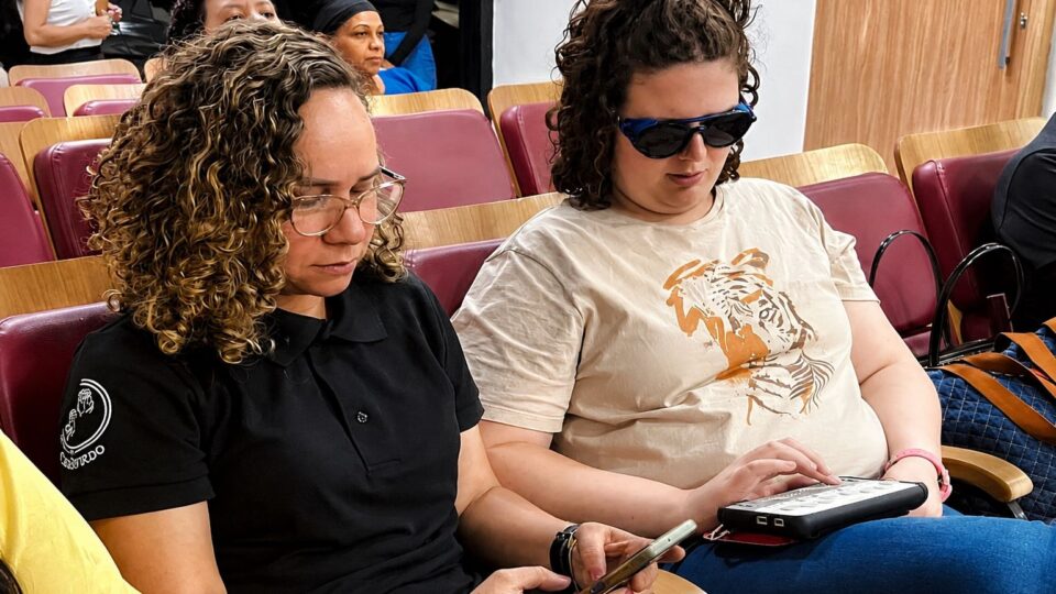 Mujer con sordoceguera y su guía-interprete comunicándose por una computadora braille. 