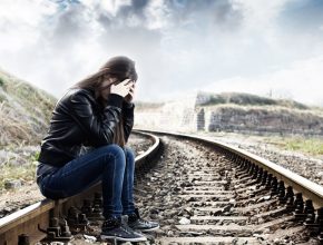 Lonely teenage girl with hands over her face sitting on the railroad