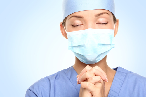 médico com máscara com mãos postas para orar