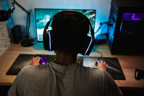 Adolescente de costas com fone de ouvido jogando no computador