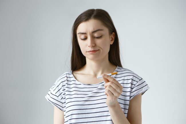 Mulher jovem segurando um cigarro e refletindo sobre como parar de fumar