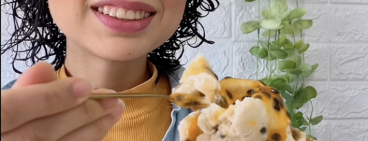Mulher sorridente segurando um cone de sorvete vegano de maracujá.