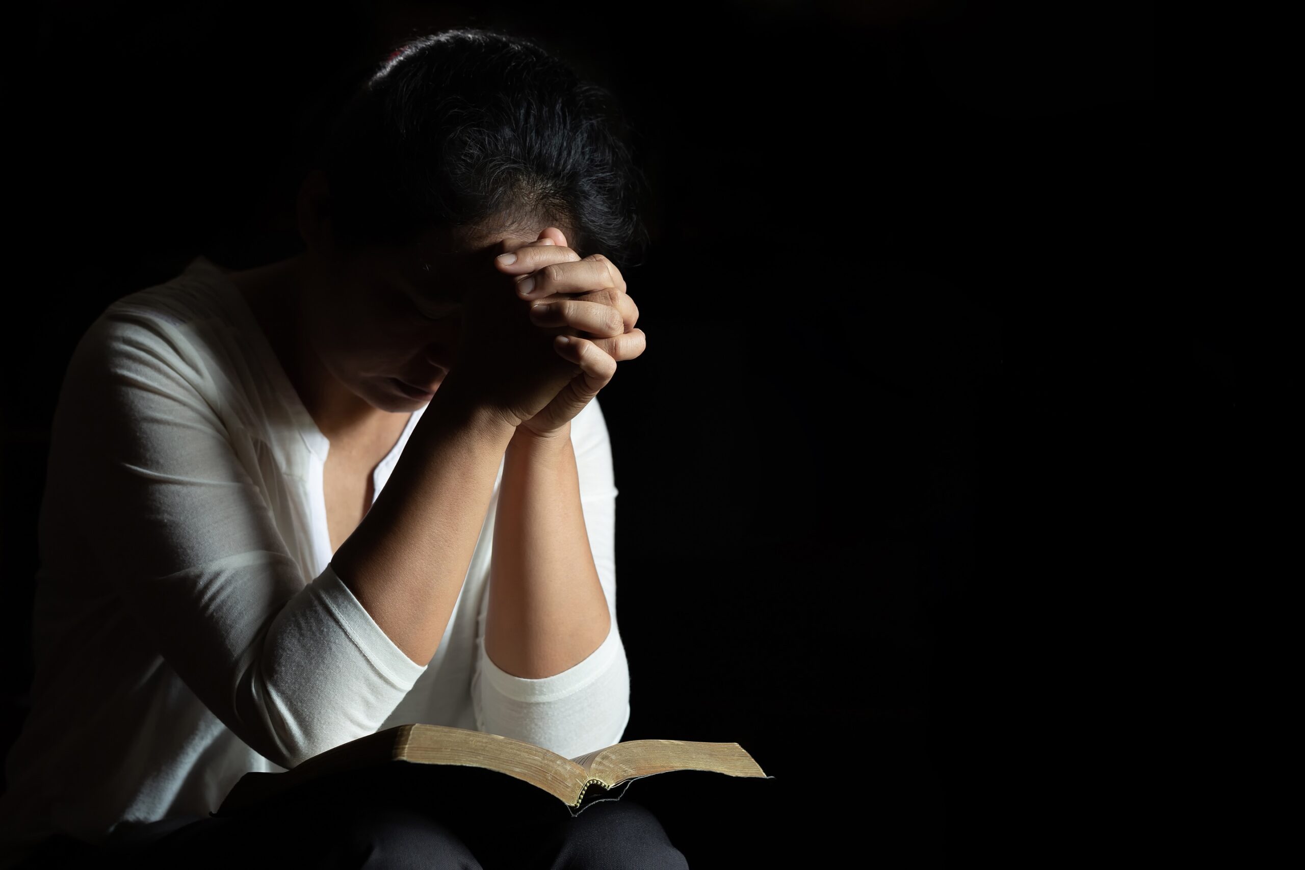 Pessoa com a cabeça baixa em oração, com uma Bíblia aberta à sua frente.