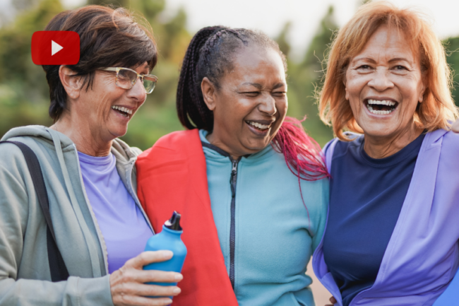 Três mulheres idosas felizes sorrindo e abraçadas ao ar livre, vestindo roupas esportivas coloridas, uma delas segurando uma garrafa de água. A imagem representa hábitos para uma vida saudável, associada ao momento vida e saúde.